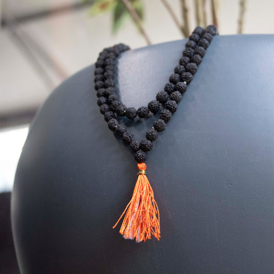 Black Rudraksha mala with orange tassel displayed on a dark surface