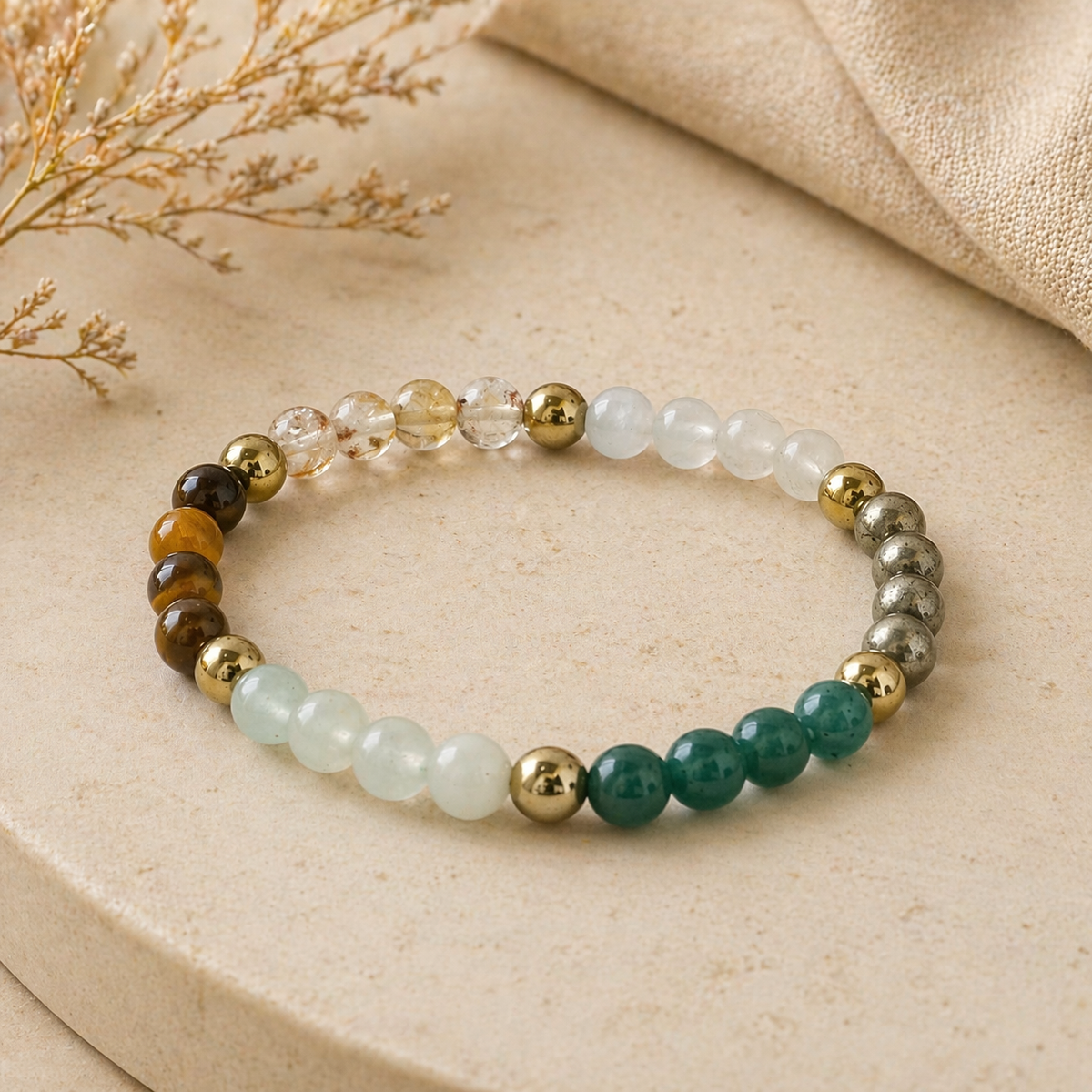 Elegant beaded stretch bracelet featuring green, gold, clear, and pyrite-toned beads on stone surface